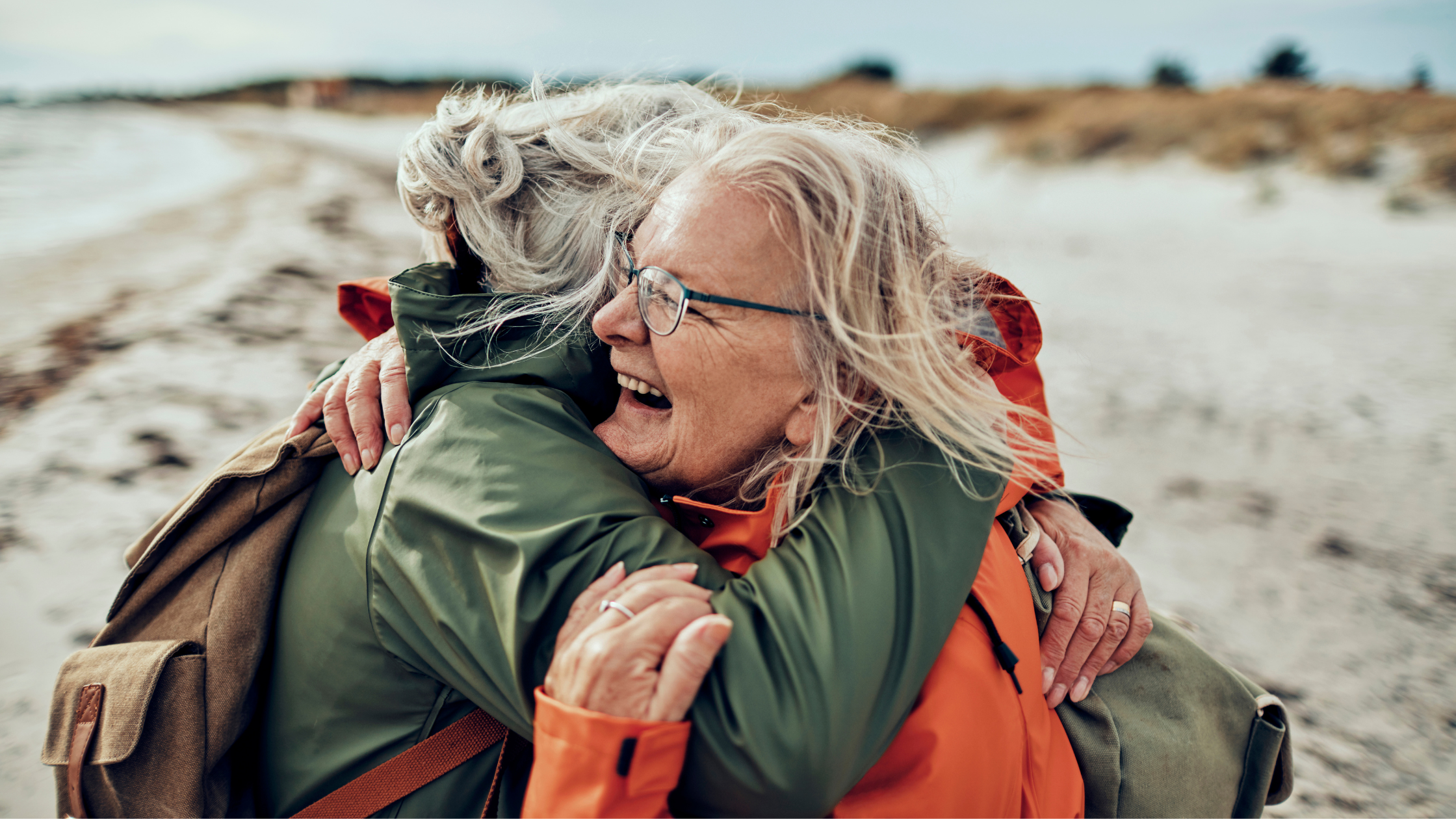 two senior women embracing on beach